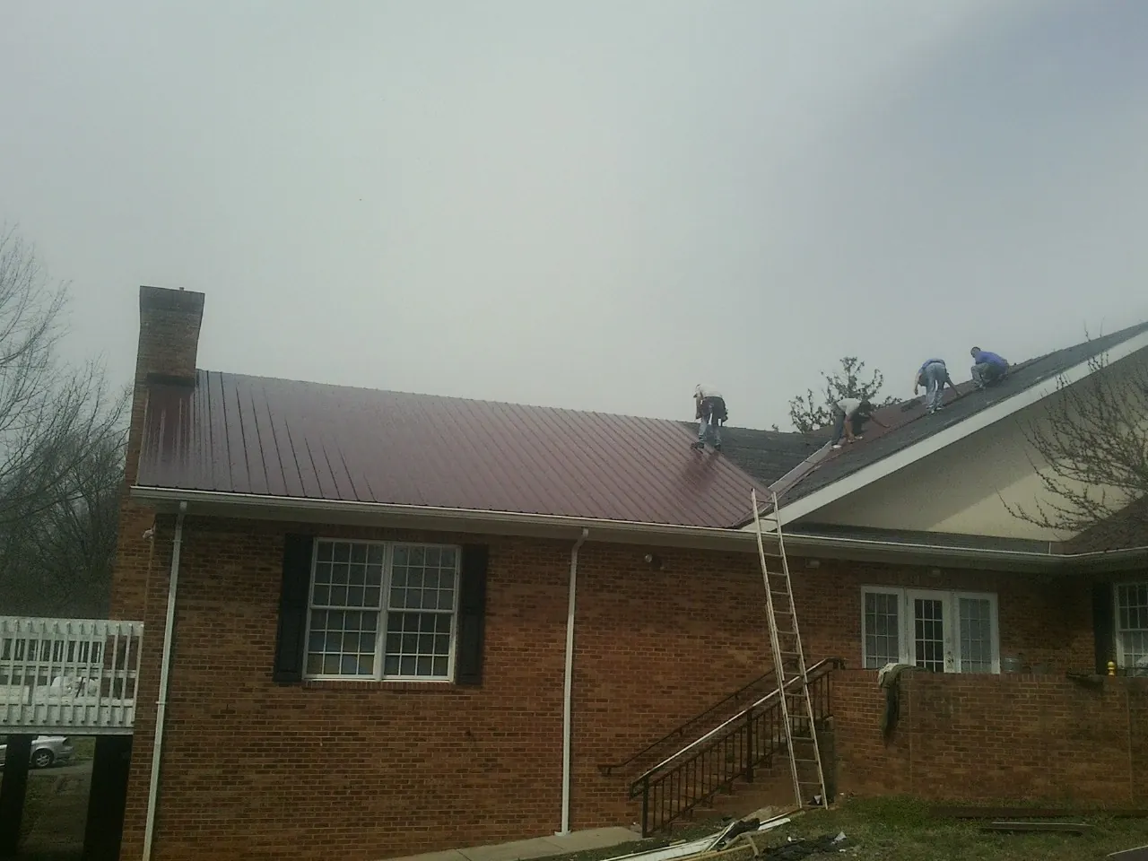 Crew setting red metal roofing panels on a brick home in Sterling