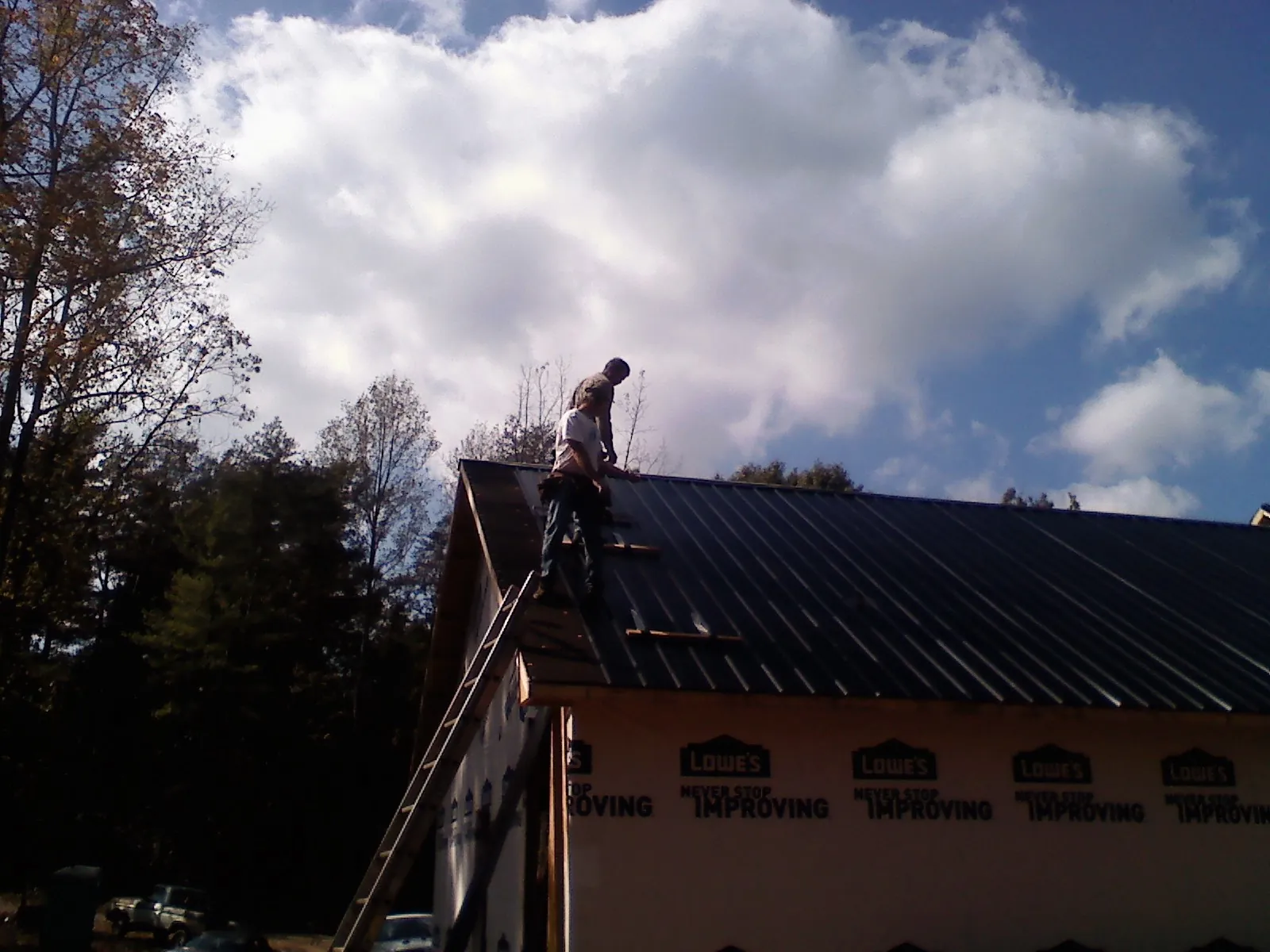 Roofer fastening dark metal panels high against a cloudy sky, from a Roof Inspection job in Sterling